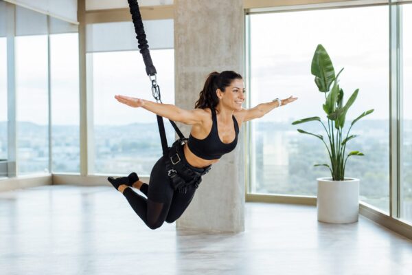 Smiling woman suspended in a bungee harness with arms outstretched during a workout in a bright studio